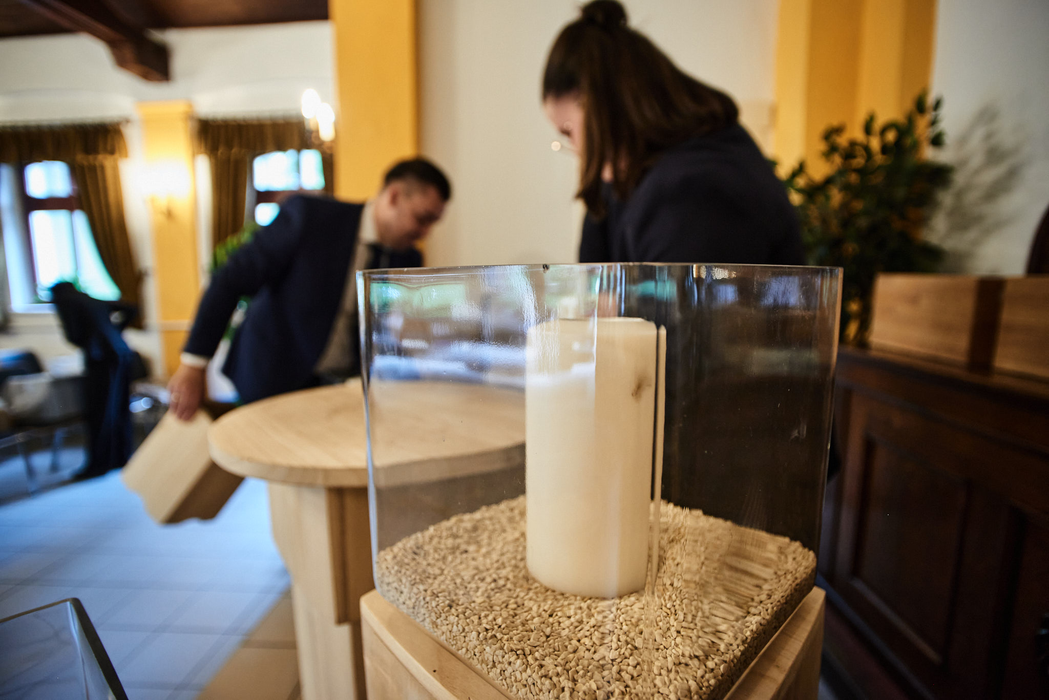 Zwei Personen bereiten einen Raum mit Holztischen und einer Kerze in Glas vor